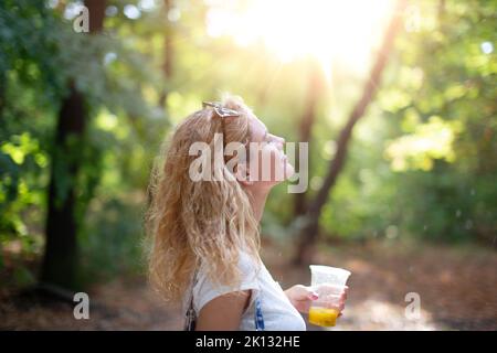 Giovane donna spensierata godendosi il sole dopo la pioggia nella natura, gli occhi chiusi Foto Stock