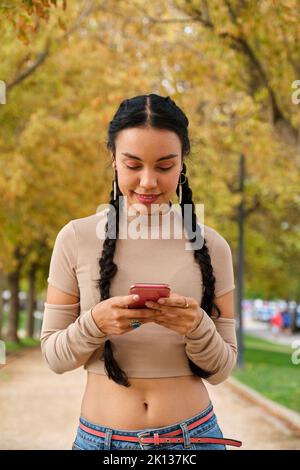 Giovane ragazza latina sorridente utilizzando lo smartphone per strada. Foto Stock