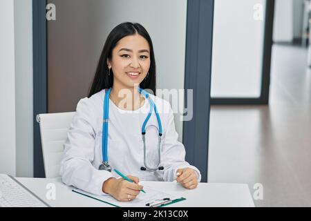 occupazione medica. Sorridente medico di medicina generale coreana seduta sul suo posto di lavoro con l'uniforme medica Foto Stock