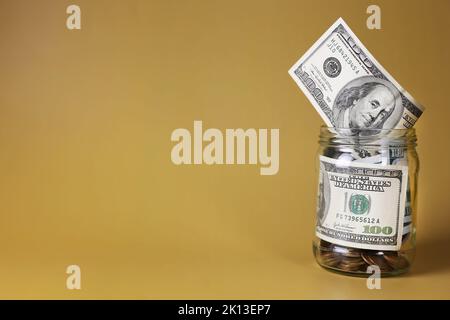 Dollari in un vaso di vetro con monete su uno sfondo giallo. Concetto di risparmio economico Foto Stock