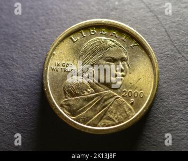 Un primo piano di una moneta dorata del dollaro di Sacagawea su una superficie grigia Foto Stock