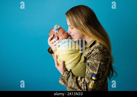 Madre Ucraina in uniforme militare con un bambino nei colori di una bandiera blu gialla durante la guerra del 2022. Primo piano in studio, fondo isolato. I più importanti eroi delle donne. Foto Stock