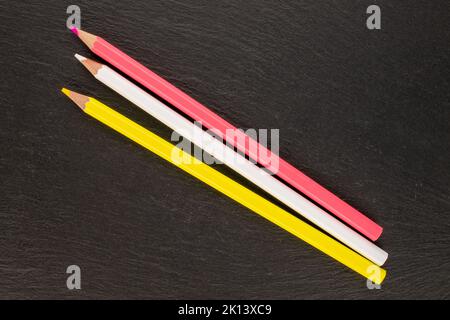Tre matite colorate su pietre di ardesia, primo piano, vista dall'alto. Foto Stock