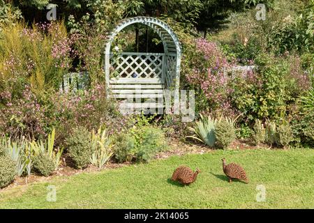 Bellissimo giardino seduta con arco in un giardino di campagna inglese con due sculture di uccelli Foto Stock