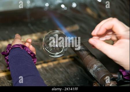 Il soffiatore di vetro riscalda il pezzo di vetro per dare forma al futuro ornamento natalizio Foto Stock