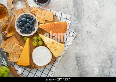 Assortimento di formaggi, miele, cracker, mirtilli, uva con vino rosso e bianco in bicchieri antipasto server su tavola di marmo bianco su fondo grigio Foto Stock