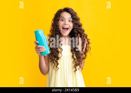 Bambina con balsami shampoo e gel doccia. Cura dei capelli lunghi dell'adolescente. Prodotto cosmetico di presentazione, bottiglia di shampoo. Adolescente eccitato Foto Stock