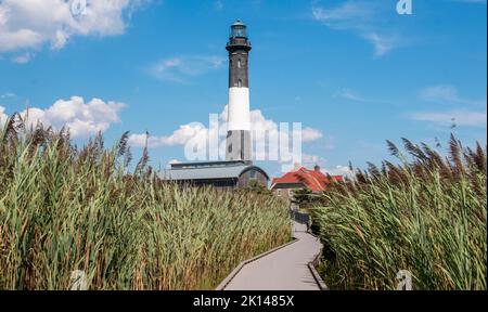 Faro di Fire Island e edificio del museo che si affaccia a est con passerella e erba da spiaggia con un cielo blu e nuvole bianche soffici Foto Stock