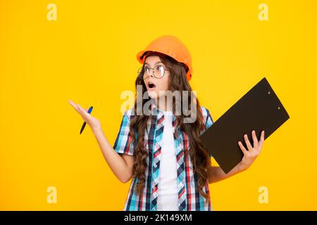 Scioccato sorpresa ragazza adolescente. Bambino pittore adolescente in casco con clipboard. Bambino in elmetto. Ingegnere di capretto sul luogo di costruzione. Ristrutturazione e. Foto Stock