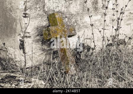 La vecchia croce di pietra è protoppata contro il muro di un tempio rovinato Foto Stock