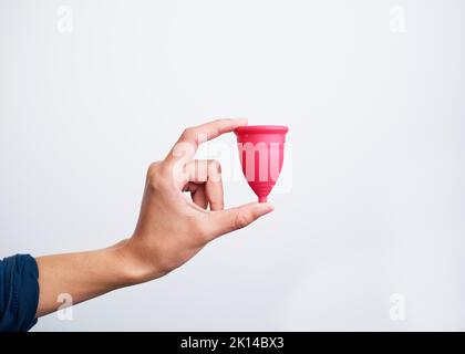 Primo piano della mano che tiene la tazza mestruale rosa su sfondo bianco Foto Stock