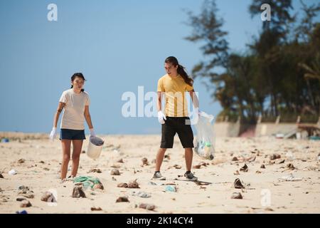 Giovane coppia che raccoglie detriti e rifiuti lasciati dai turisti sulla spiaggia Foto Stock