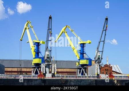 Gru portuali dipinte nei colori della bandiera Ucraina, giallo e blu, sfondo cielo blu Foto Stock