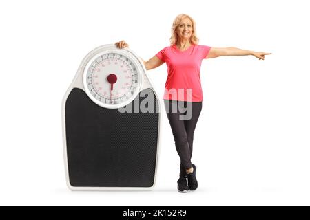Ritratto a tutta lunghezza di una donna matura in abbigliamento sportivo che posa con una grande misura e che punta al lato isolato su sfondo bianco Foto Stock