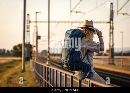 Viaggi in vacanza. Donna con zaino in attesa di treno alla stazione ferroviaria Foto Stock