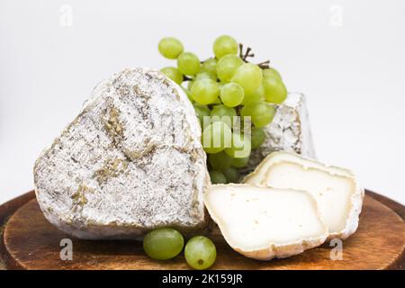 Formaggi blu piccanti assortiti latte di capra su un tagliere di legno con uve verdi. Sfondo bianco. Foto Stock