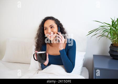 Una giovane donna multietnica ride mentre si chiama da letto Foto Stock