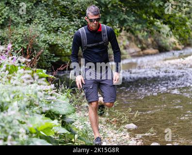 Uomo maturo escursionista a piedi nella foresta accanto al fiume di montagna Foto Stock