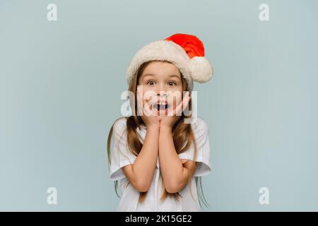 Piccola ragazza sorpresa in santa Hat dice wow e guarda la macchina fotografica. Vendite di Natale. Foto Stock