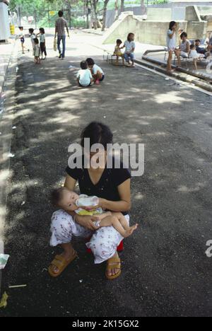 Una donna vietnamita nutre il bambino con una bottiglia in un campo profughi a Kai Tak, Hong Kong. Foto Stock