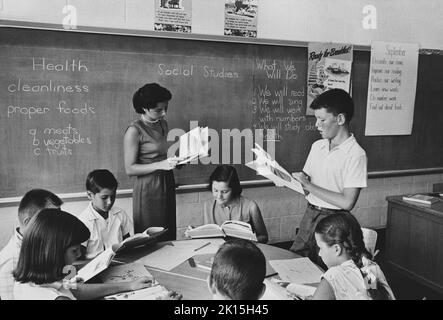 L'insegnante e gli altri studenti di una classe di quinto grado ascoltano mentre un ragazzo legge ad alta voce. Yonkers, Queens, New York. Circa anni '50, anni '60, Foto Stock