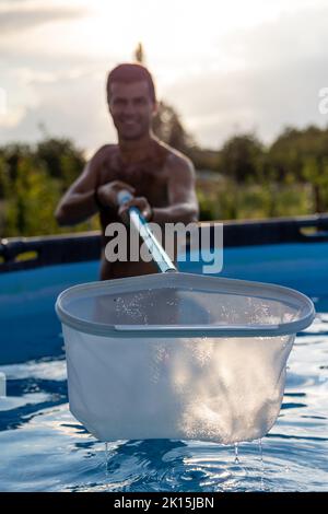 Uomo in piscina che pulisce una certa sporcizia dall'acqua con l'apparecchiatura della rete Foto Stock