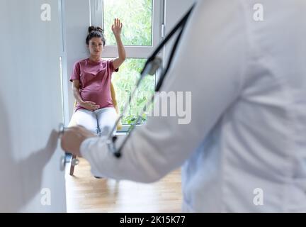 Vista posteriore del medico che chiama una donna incinta in sala d'attesa per un appuntamento Foto Stock