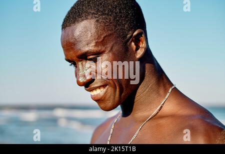 Felice uomo afroamericano con catena argentata sul collo sorridente su sfondo sfocato del mare e cielo azzurro nuvoloso in estate Foto Stock