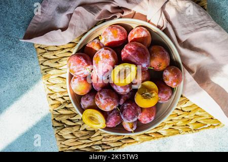 Frutti di prugna freschi, biologici e maturi nel recipiente su fondo in cemento Foto Stock