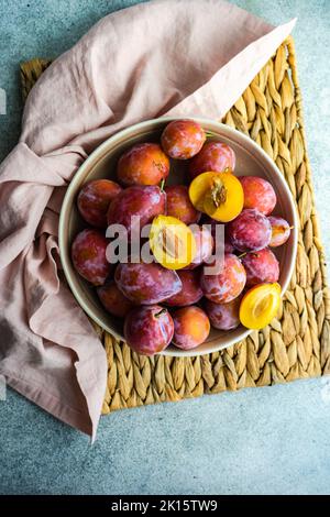 Frutti di prugna freschi, biologici e maturi nel recipiente su fondo in cemento Foto Stock