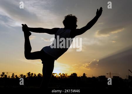 Silhouette di irriconoscibile Dandayamana Dhanurasana posa contro cielo nuvoloso tramonto durante la sessione di yoga di sera Foto Stock