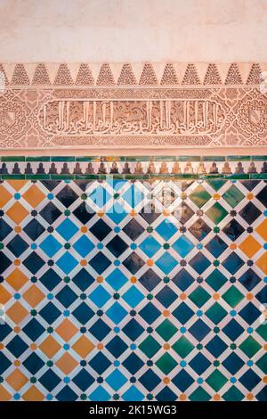 Tessere mosaico colorate che formano ornamento geometrico sotto iscrizione araba sulla parete del vecchio palazzo del complesso fortezza dell'Alhambra a Granada, Spagna Foto Stock