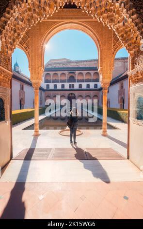 Donna anonima in piedi sotto l'arco vicino alla tranquilla piscina e tiro al sole Corte dei Myrtles di Comares Palace il giorno del fine settimana a Granada, Spagna Foto Stock