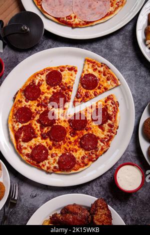 Vista dall'alto del piatto con deliziosa pizza peperoni e ciotola di salsa posta sul tavolo grigio durante il pranzo Foto Stock