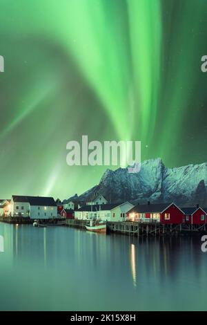 Spettacolare vista di vivide luci polari verdi che brillano nel cielo sulle case residenziali situate nelle Highlands vicino al lago in Norvegia di notte Foto Stock