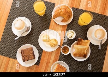 Vista dall'alto di vari tipi di pasticcini e bevande, posti vicino a bocce con salse sul tavolo durante la colazione nel ristorante Foto Stock