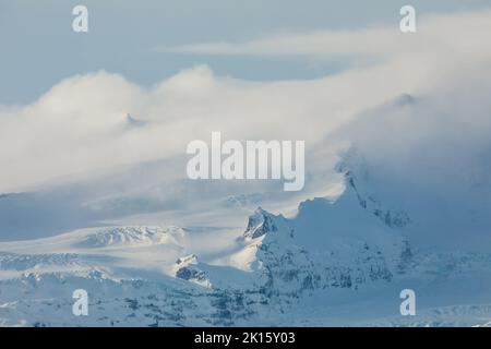 Nuvole bianche spesse che galleggiano nel cielo blu sopra la cresta innevata della montagna nella fredda giornata invernale in Islanda Foto Stock