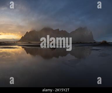 Spettacolare vista dell'acqua calma e della montagna di Vestrahorn situata contro il cielo nuvoloso dell'alba in inverno mattina in Islanda Foto Stock