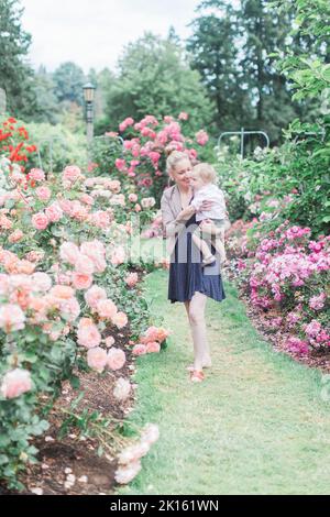 La madre caucasica di 30 anni tiene il figlio del toddler nel giardino di rosa. Foto Stock