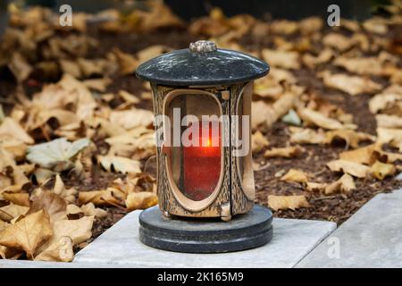 lanterna commemorativa con candela accesa su una tomba con foglie autunnali Foto Stock