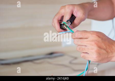 L'elettricista taglia i fili elettrici con le pinze, installazione cavi elettrici per spina di presa. Riparazione, ristrutturazione, riparazione, assistenza e sviluppo della casa Foto Stock