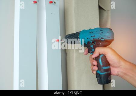 Uomo che utilizza un avvitatore a batteria che monta mobili a casa, Carpenter che lavora con un avvitatore elettrico sul lavoro Foto Stock