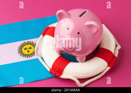 Piggy bank, lifboa e bandiera su uno sfondo colorato, il concetto di salvare l'economia argentina Foto Stock