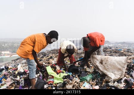 Gruppo di bambini di strada senza tetto che raccolgono rifiuti in una discarica fumante in una metropoli africana; concetto di povertà e di negligenza dei bambini Foto Stock