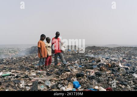 Tre ragazzi africani esposti a lesioni e malattie gravi alla ricerca di articoli usabele in un grande junkyard urbano; concetto di mancanza di igiene e salute Foto Stock