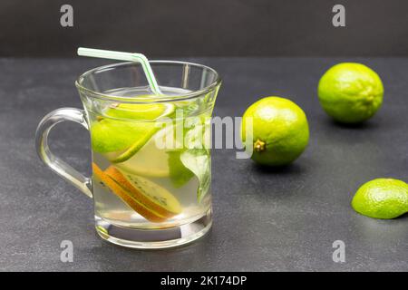 Bevanda al limone con basilico verde in un bicchiere. Limes sul tavolo. Sfondo nero Foto Stock