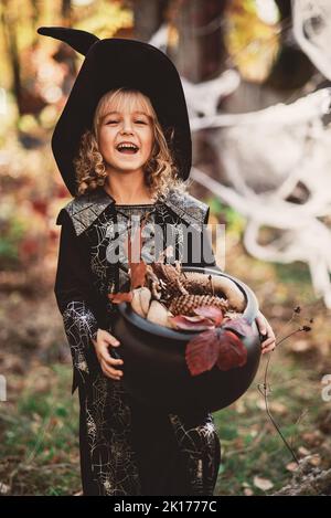 Ragazza bella strega. Bambina in cui il costume celebra Halloween all'aperto e Buon divertimento. Capretti trucco o trattando. Strega della ragazza con il libro magico degli incantesimi. Foto Stock