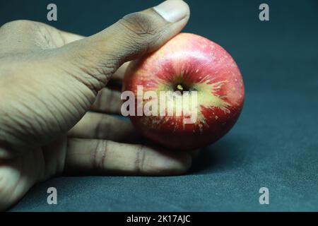 Mani che tengono una mela rossa, la mela proibita, su sfondo nero. Foto Stock