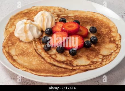 Frittelle con fragole, mirtilli, panna e sciroppo d'acero sul piatto Foto Stock