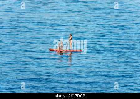 Due donne mature, una in piedi e l'altra seduta su una tavola da paddle stand up o paddleboard (SUP) nel Mar Mediterraneo. Liguria, Italia. Foto Stock